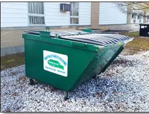 A green dumpster sitting in the middle of a gravel yard.